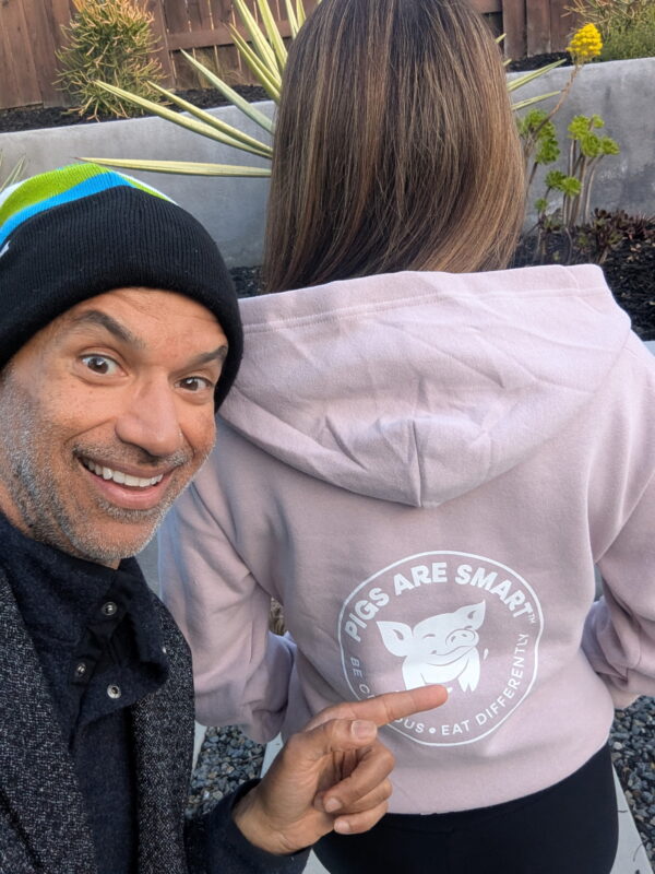 Man smiling and pointing at the back of a woman’s Pigs Are Smart hoodie, featuring the logo and tagline.